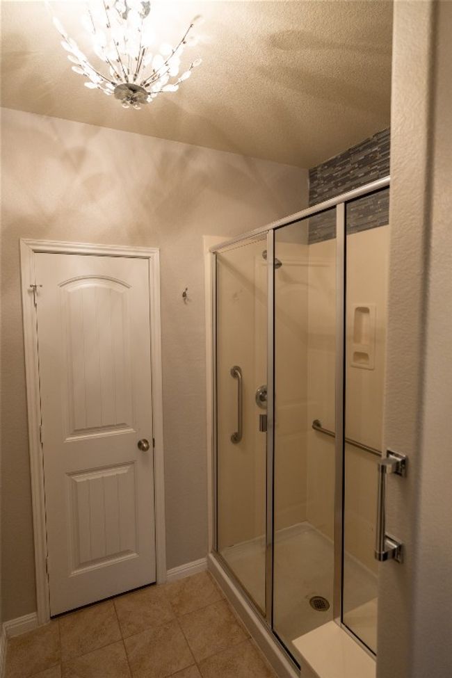 Full bath featuring a shower stall, tile patterned flooring, a chandelier, a textured ceiling, and baseboards | Image 10
