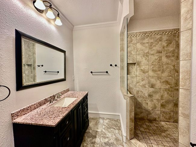Full bath with vanity, walk in shower, crown molding, a textured wall, and a textured ceiling | Image 9