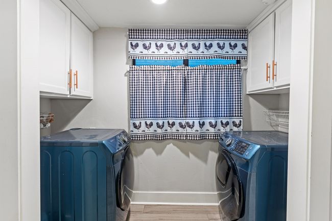 Laundry area featuring washing machine and clothes dryer, cabinet space, baseboards, and light wood-style flooring | Image 23