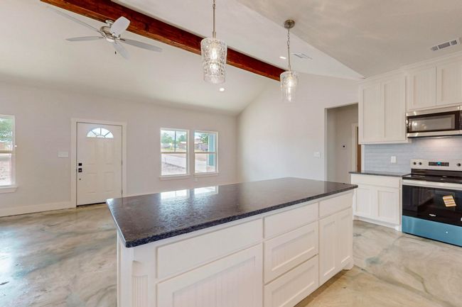 Kitchen featuring appliances with stainless steel finishes, backsplash, a kitchen island, decorative light fixtures, and white cabinets | Image 23