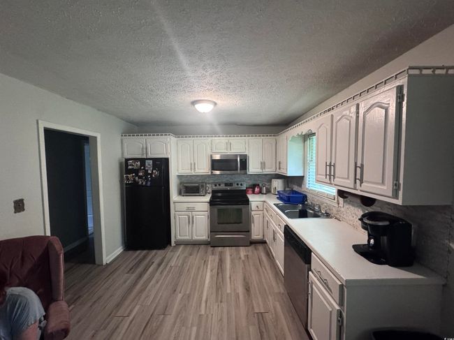 Kitchen featuring stainless steel appliances, a sink, light countertops, light wood-type flooring, and backsplash | Image 11