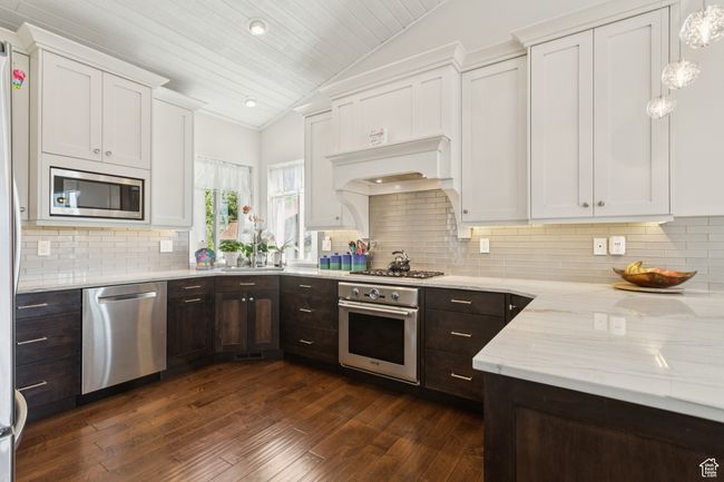 Kitchen featuring appliances with stainless steel finishes, vaulted ceiling, white cabinetry, dark brown cabinets, and dark wood-style flooring | Image 5