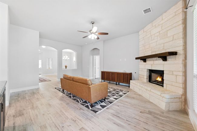 Living room with ceiling fan, a stone fireplace, arched walkways, and light wood-type flooring | Image 11