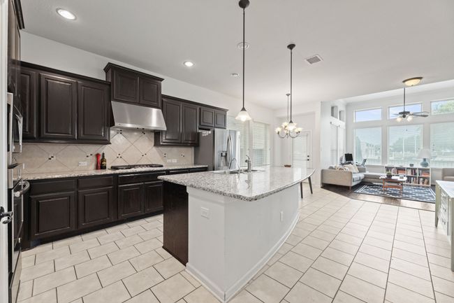 Kitchen featuring under cabinet range hood, appliances with stainless steel finishes, open floor plan, light tile patterned floors, and a sink | Image 7