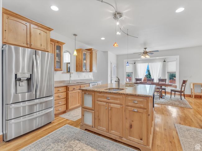 Kitchen with a sink, an island with sink, glass insert cabinets, stainless steel fridge with ice dispenser, and light wood-style flooring | Image 11