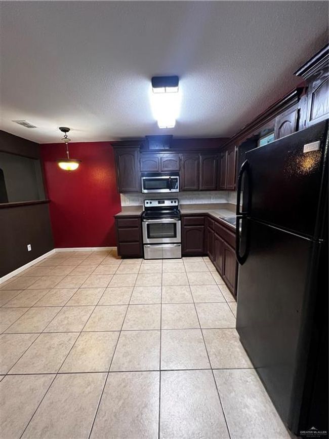 Kitchen featuring refrigerator, stainless steel electric stove, light tile patterned floors, light countertops, and a textured ceiling | Image 4