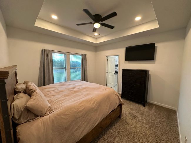 Bedroom featuring light colored carpet, a decorative wall, a crib, a ceiling fan, and wainscoting | Image 4