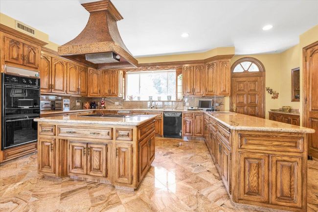 Kitchen featuring a center island, backsplash, marble finish floor, black appliances, and custom exhaust hood | Image 7