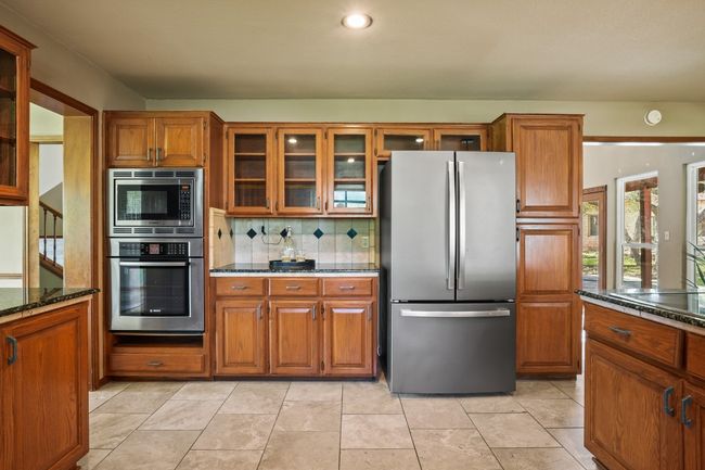Kitchen with stainless steel appliances, brown cabinetry, glass insert cabinets, and tasteful backsplash | Image 6