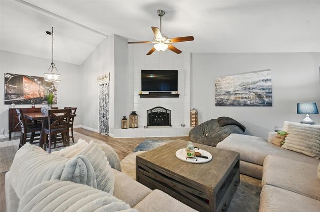 Living room featuring ceiling fan, vaulted ceiling, wood finished floors, a chandelier, and a tiled fireplace | Image 6