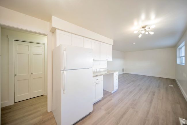 Kitchen with white cabinets, light wood-type flooring, white refrigerator, and light stone countertops | Image 5