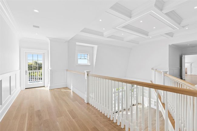 Unfurnished living room featuring a decorative wall, a high ceiling, built in features, a warm lit fireplace, and light wood finished floors | Image 17