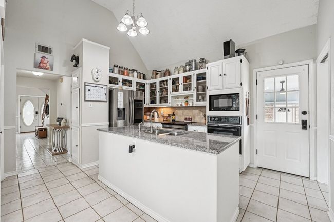 Kitchen with black appliances, light tile patterned floors, backsplash, high vaulted ceiling, and white cabinetry | Image 11