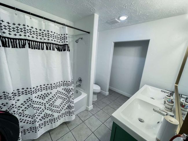 Full bath featuring a textured ceiling, tile patterned floors, shower / bath combo with shower curtain, toilet, and vanity | Image 21