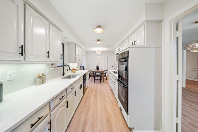 Kitchen featuring quartz countertops, a farm sink, light wood-style flooring, black dishwasher, and a tile backsplash | Image 7