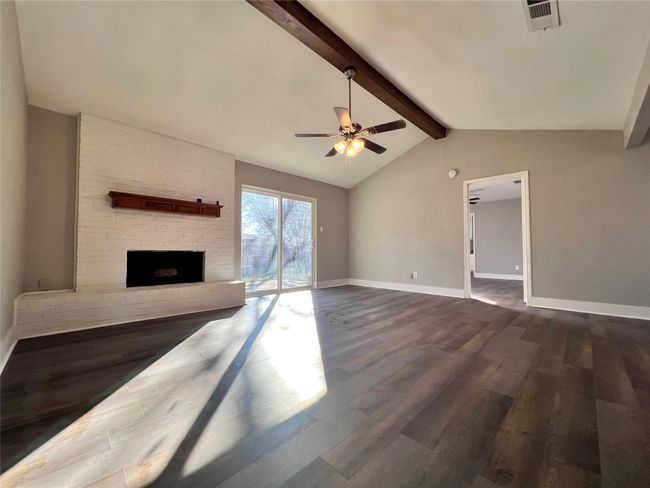 Unfurnished living room with ceiling fan, dark wood-type flooring, lofted ceiling with beams, and a brick fireplace | Image 5