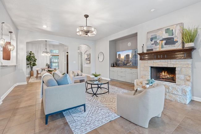 Living room featuring arched walkways, a chandelier, baseboards, a stone fireplace, and tile floors | Image 9