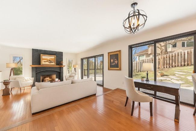 Sun-filled living room with a cozy fireplace and adjacent office nook, overlooking a beautifully landscaped, snow-free backyard through expansive glass doors. (partially virtually staged) | Image 8