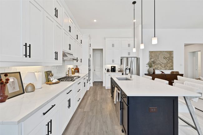 Kitchen with stainless steel appliances, a sink, under cabinet range hood, backsplash, and white cabinets | Image 17