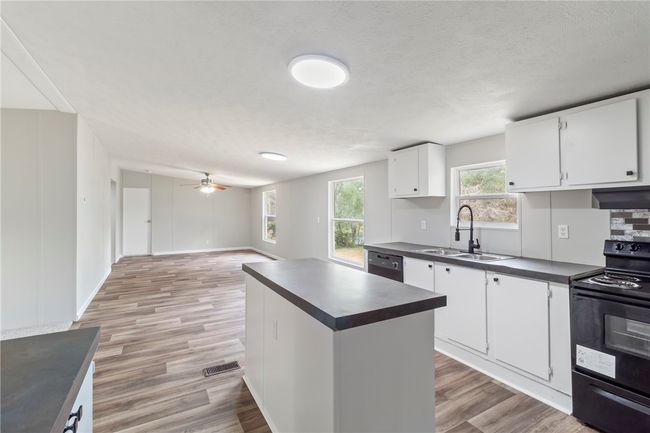 Kitchen with black appliances, dark countertops, a sink, and light wood-type flooring | Image 10