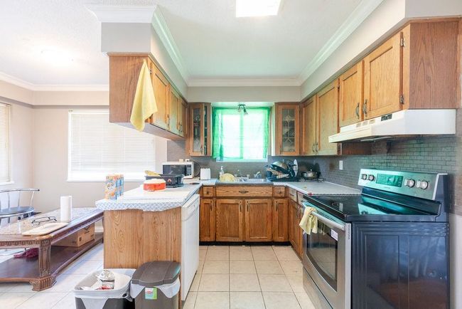 Kitchen with stainless steel appliances, under cabinet range hood, light tile patterned floors, decorative backsplash, and crown molding | Image 7