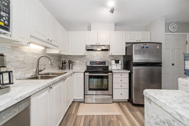 Kitchen with under cabinet range hood, a sink, tasteful backsplash, white cabinetry, and stainless steel appliances | Image 10