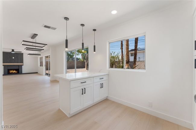 Kitchen with a peninsula, white cabinetry, light wood-style floors, a warm lit fireplace, and light countertops | Image 20