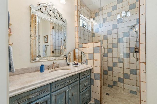 The "Provence Full Bath Ensuite, the flooring is Artisan Azul Chateau Decor 13"x13" ceramic tile by Mercola Tile. Custom-designed and crafted vanity cabinetry, with a base color of "French Moire" in a vintage distressed style designed to replicate an antique dresser. | Image 35