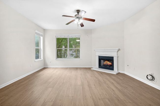 Unfurnished living room with wood finished floors, a ceiling fan, and a warm lit fireplace | Image 7
