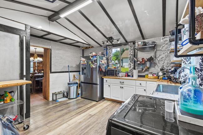Kitchen with stainless steel fridge, a sink, a chandelier, white cabinets, and light wood-type flooring | Image 12