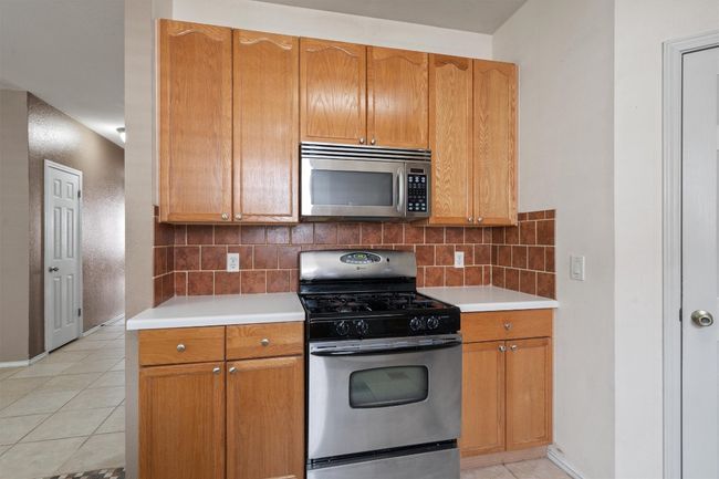 Kitchen with stainless steel appliances, light countertops, decorative backsplash, and light tile patterned flooring | Image 17