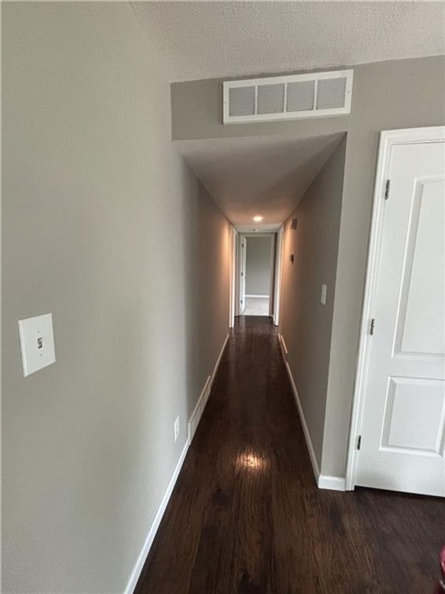 Hallway featuring dark wood finished floors, visible vents, a textured ceiling, and baseboards | Image 27