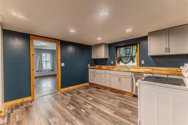 Kitchen with white range with electric stovetop, a sink, butcher block counters, baseboards, and dishwashing machine | Image 14