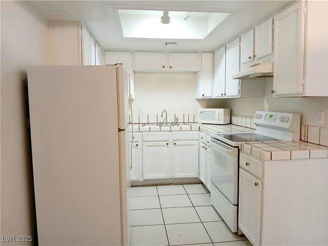 Kitchen with white appliances, tile counters, and white cabinets | Image 4