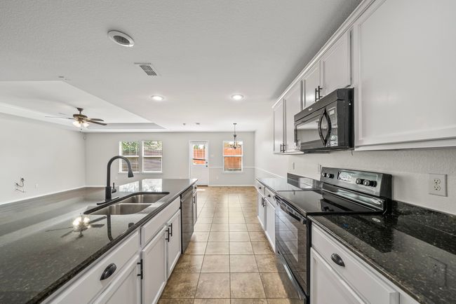 Kitchen with black appliances, light tile patterned flooring, white cabinetry, recessed lighting, and dark stone countertops | Image 14