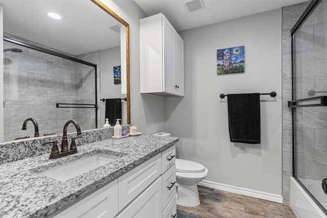Full bath featuring wood finished floors, baseboards, vanity, toilet, and enclosed tub / shower combo | Image 6