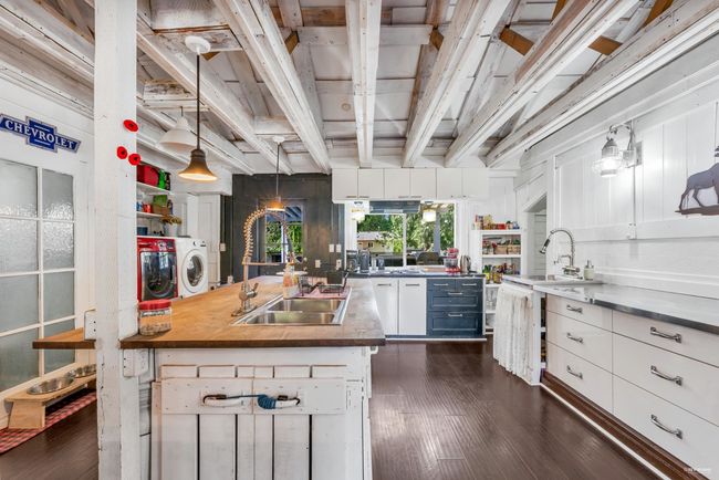 Kitchen with white cabinets, a sink, decorative light fixtures, washer and dryer, and dark wood-style flooring | Image 10