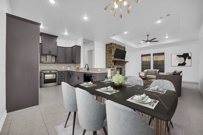 Tiled dining room featuring a stone fireplace, ceiling fan with notable chandelier, and a raised ceiling | Image 6