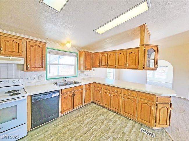 Kitchen featuring light wood-style floors, black dishwasher, white electric range, visible vents, and a peninsula | Image 9