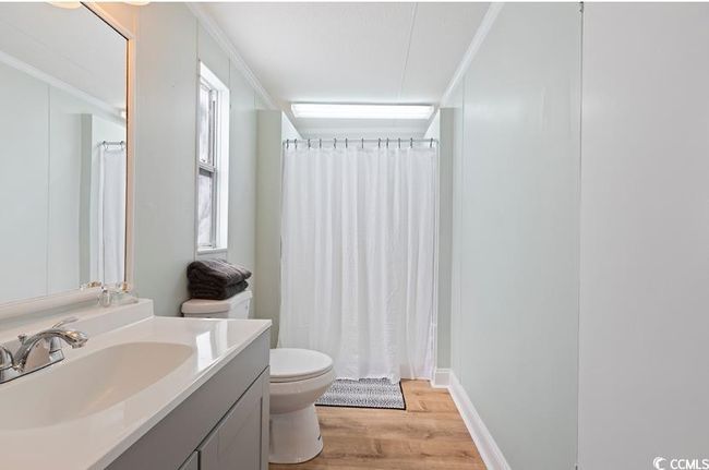 Bathroom featuring toilet, vanity, wood finished floors, crown molding, and curtained shower | Image 23