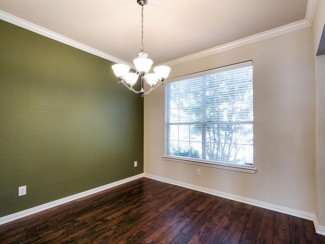 Empty room with dark wood-style flooring, a chandelier, baseboards, and ornamental molding | Image 12