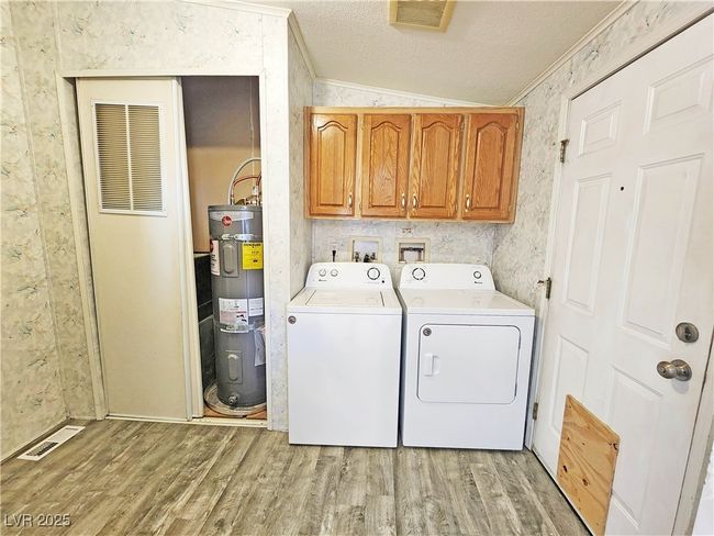 Clothes washing area featuring visible vents, ornamental molding, light wood-type flooring, and electric water heater | Image 27