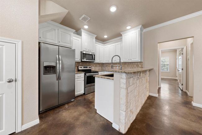 Kitchen with stainless steel appliances, concrete floors, backsplash, white cabinets, and recessed lighting | Image 5