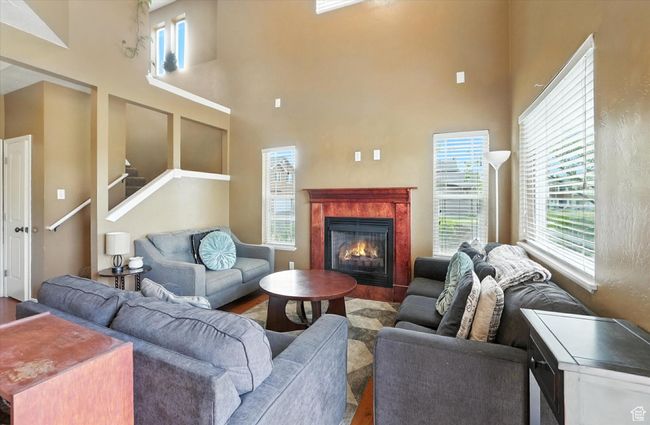 Living area with wood finished floors, a high ceiling, healthy amount of natural light, a fireplace, and stairway | Image 5