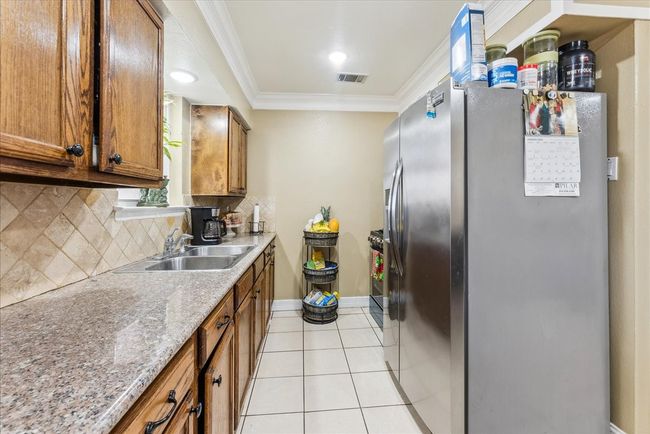 Kitchen featuring crown molding, a sink, stainless steel fridge with ice dispenser, light tile patterned floors, and visible vents | Image 6