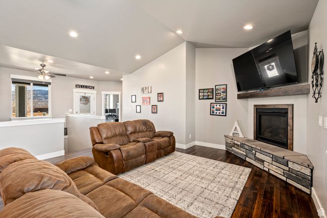 Living room with dark wood finished floors, a stone fireplace, recessed lighting, lofted ceiling, and baseboards | Image 8
