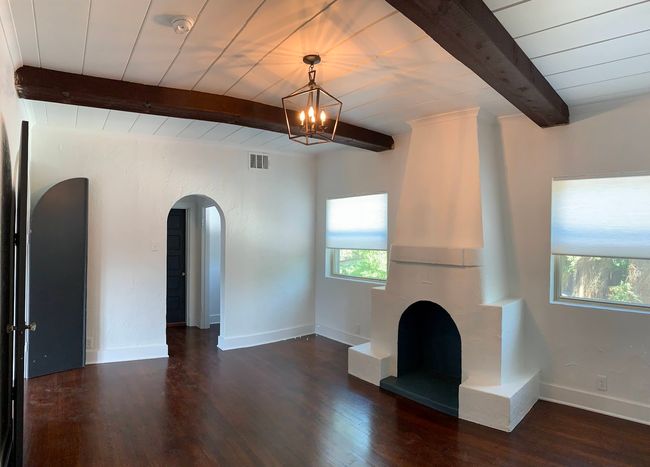 Unfurnished living room featuring arched walkways, a chandelier, dark wood-type flooring, a wooden ceiling with exposed beams, and a fireplace with raised hearth | Image 7