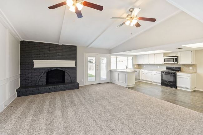 Unfurnished living room with a brick fireplace, lofted ceiling, carpet flooring, and a ceiling fan | Image 14