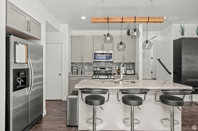 Kitchen featuring stainless steel appliances, dark wood-style floors, a breakfast bar area, and a textured ceiling | Image 11