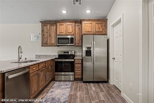 Kitchen featuring appliances with stainless steel finishes, a sink, dark wood-style flooring, a peninsula, and brown cabinets | Image 30